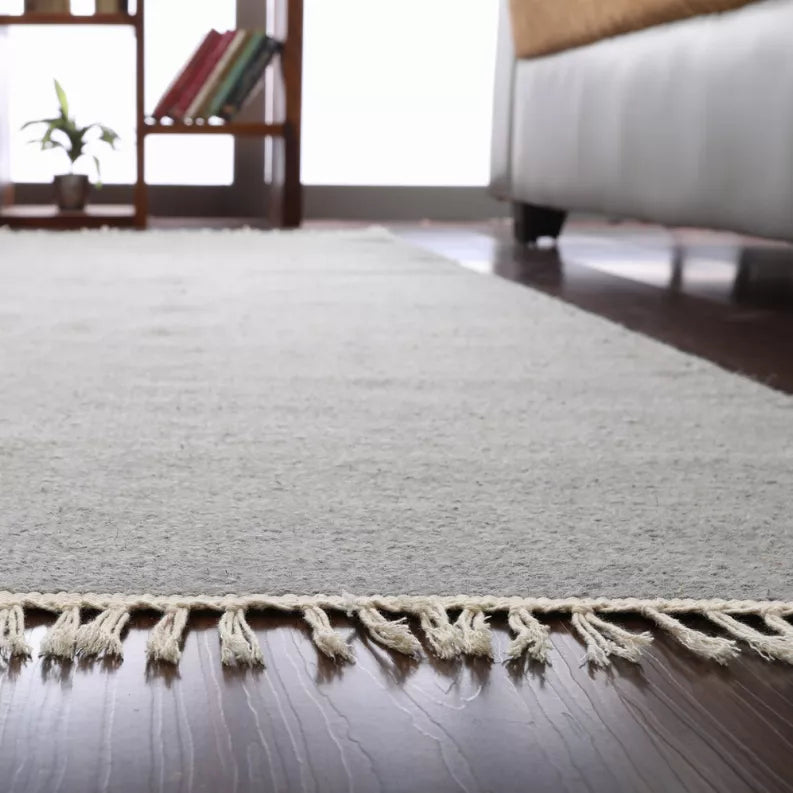 Gray rug edge with cream tassel fringe, close-up along border