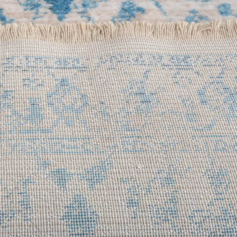 Close-up rug edge with cream and light-blue patterning and fringe along the border.