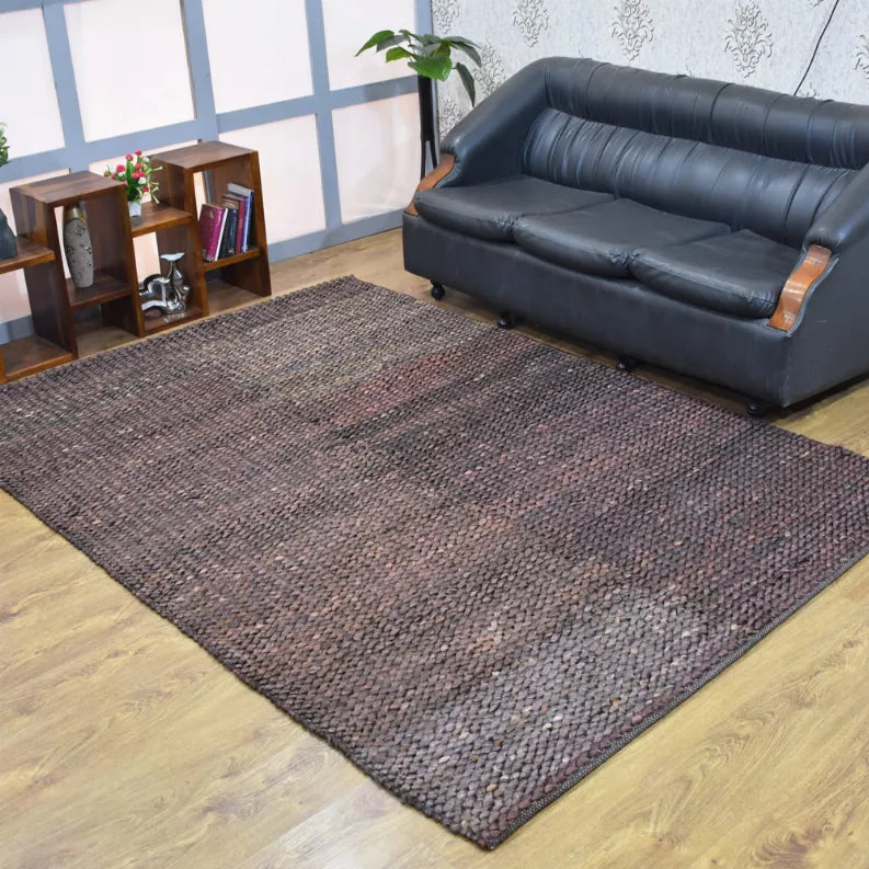 Hand-woven jute area rug laid flat on hardwood floor, solid dark gray-brown tone