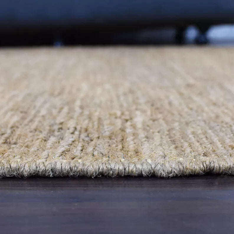 Beige jute area rug edge with short fringe-like fibers along the border