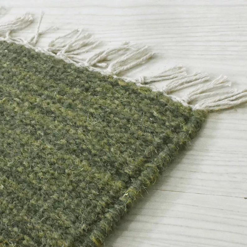 Olive green hand-woven wool kilim rug with white fringe along the border