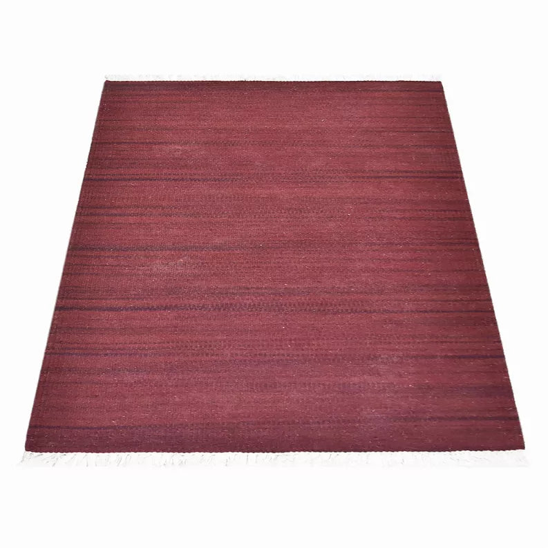 Solid burgundy handwoven wool kilim rug with flat weave texture and white fringe edges.