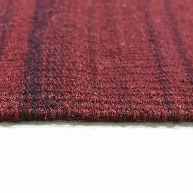 Burgundy wool rug end with dense flat weave texture and finished border