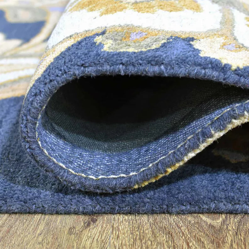 Folded edge of hand-tufted wool rug showing dark backing and blue bound border trim.
