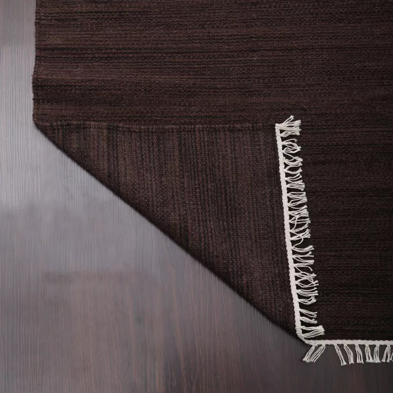 Dark brown flat weave rug with cream fringe on a corner edge.