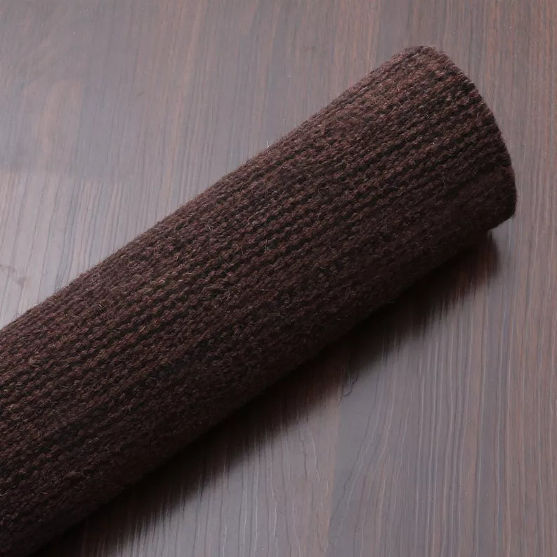 Dark brown rug rolled along the side edge, showing dense flat weave texture.