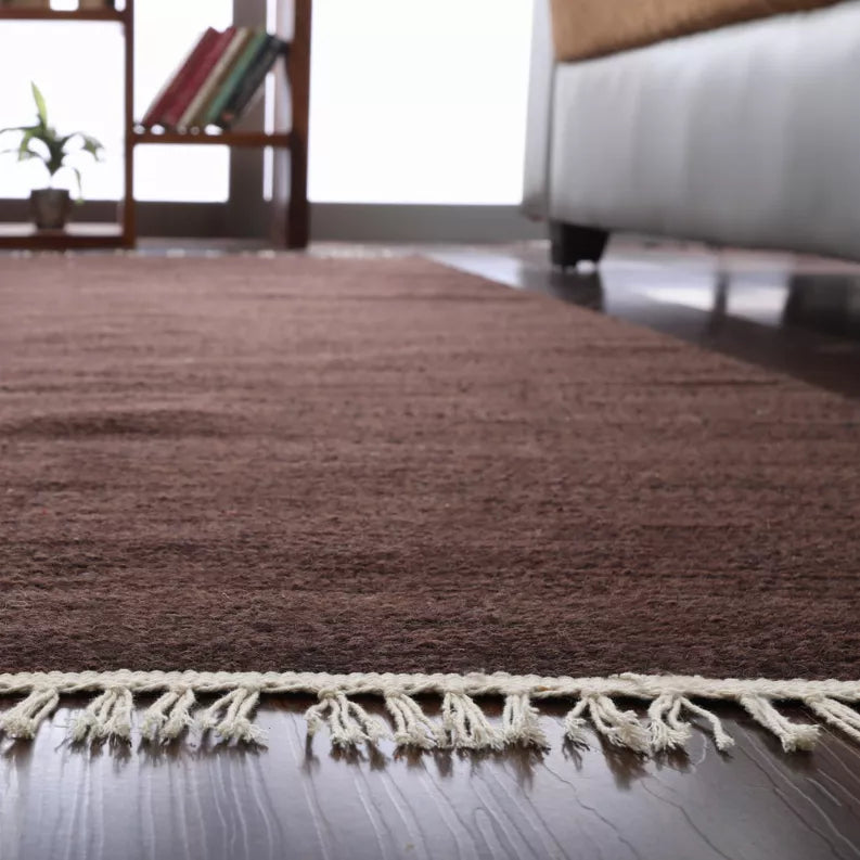 Dark brown flat weave rug with cream fringe trim along the edge.