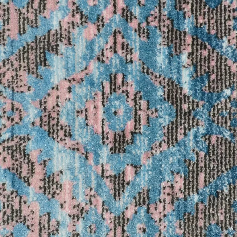 Rug detail showing blue and pink geometric motif with dark charcoal crossweave texture.