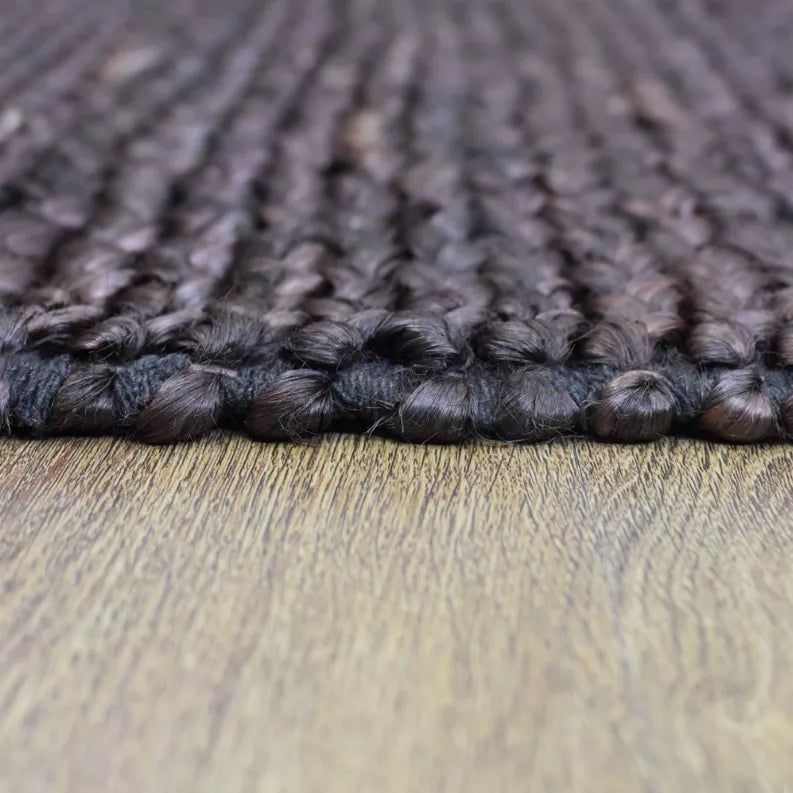 Hand-woven jute rug close-up of braided pile, dark gray with subtle pink flecks