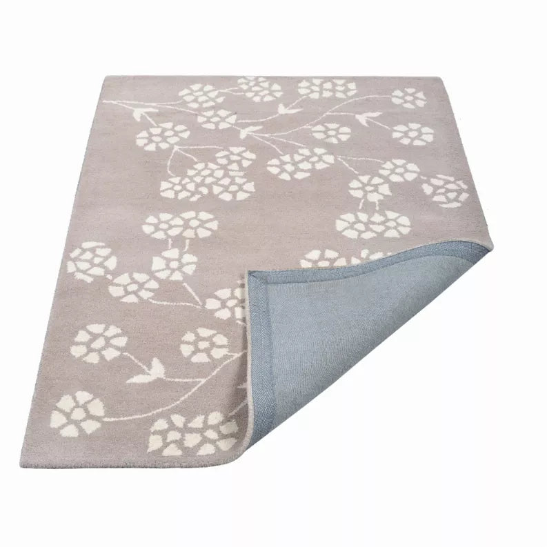 Hand tufted wool area rug with white floral vines on light taupe, folded corner reveals blue backing