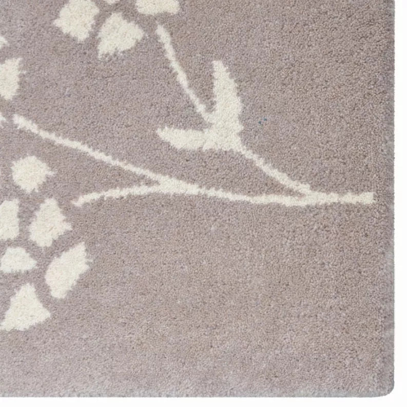 Taupe rug corner with white vine line and floral rosette, close-up