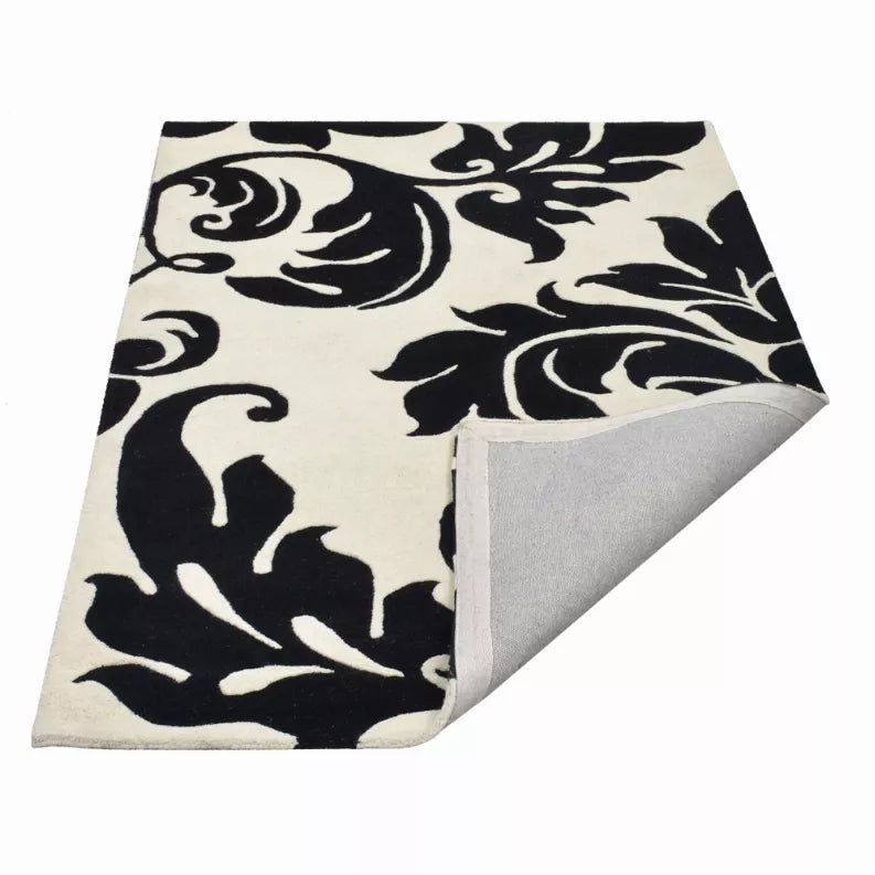 Black and ivory floral area rug with ornate swirls, corner with gray backing visible