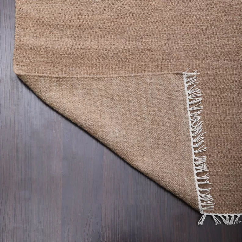 Tan wool flatweave kilim rug corner with trimmed fringe and woven texture