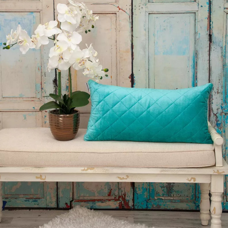 Turquoise quilted throw pillow on a bench with diamond stitching and a piped edge.
