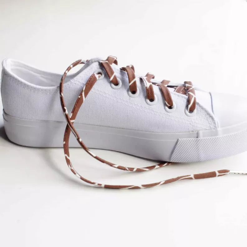Giraffe-print shoelaces with aglets on a white sneaker side view, laid out.
