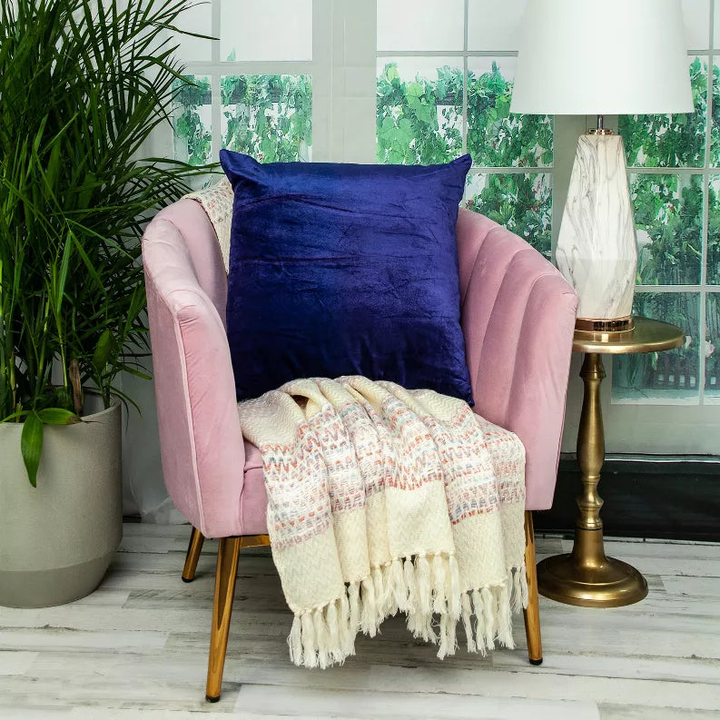 Royal blue solid throw pillow on a chair with a knit throw blanket in front.