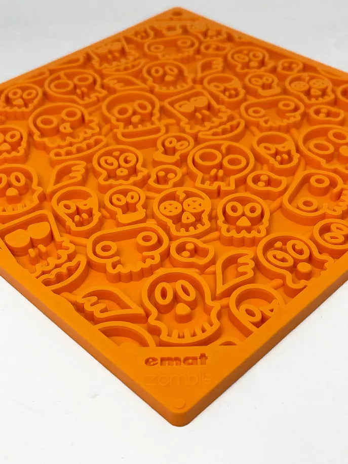 Orange rubber lick mat with raised zombie face and skull shapes, top view