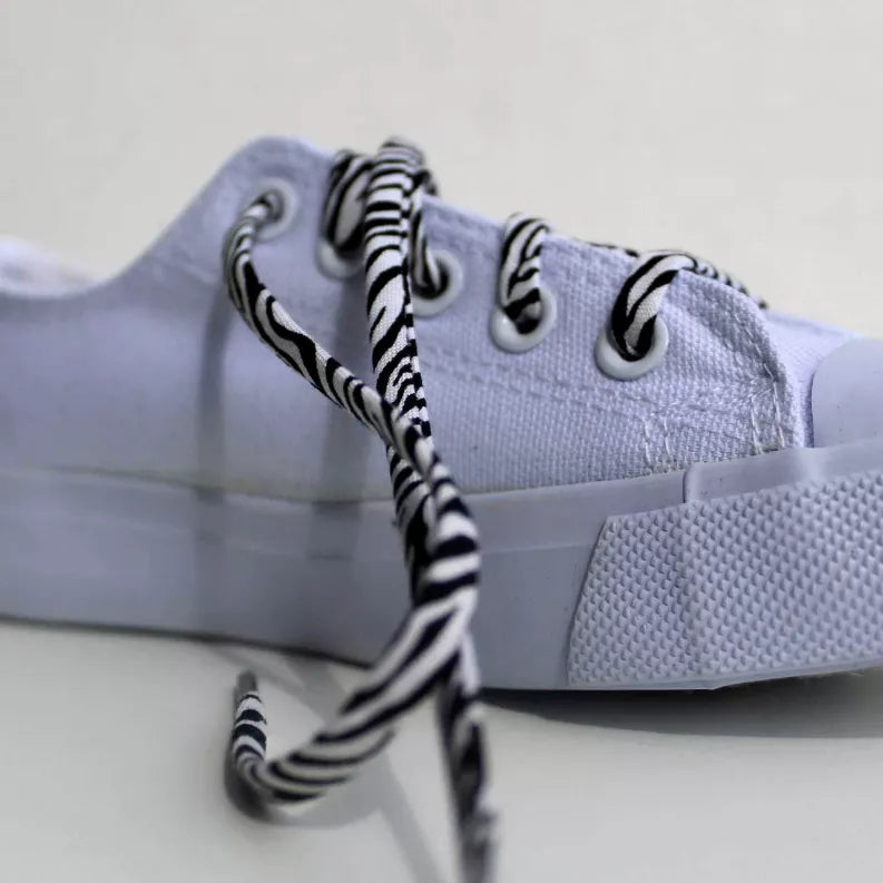 Zebra-print laces threaded on light gray sneaker eyelets, striped black and white