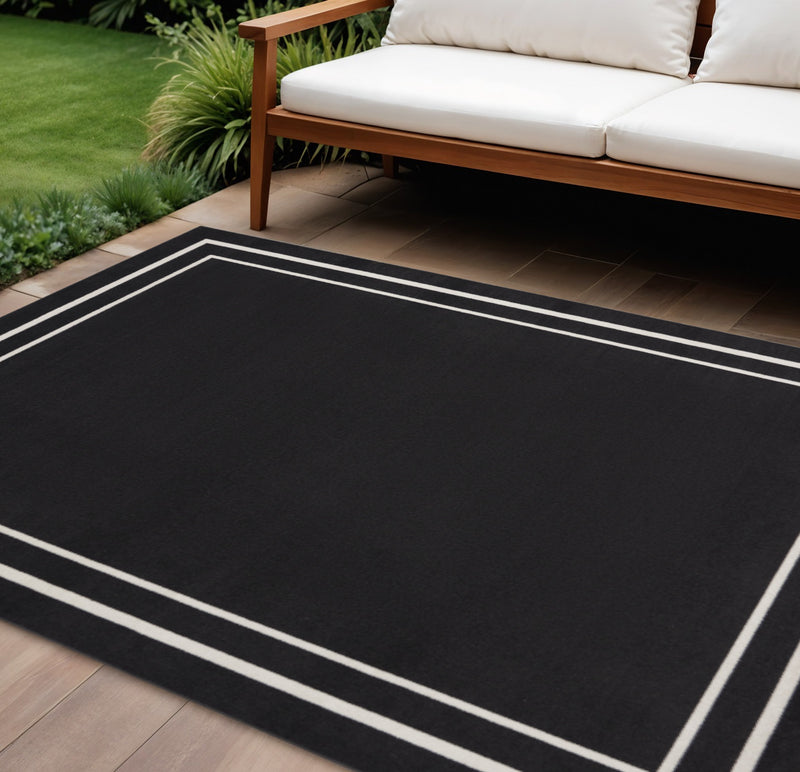 Black indoor/outdoor area rug with bold ivory double-line border on a flat surface.