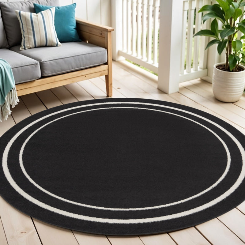 Round black area rug with ivory concentric circle pattern, low-pile for indoor/outdoor use
