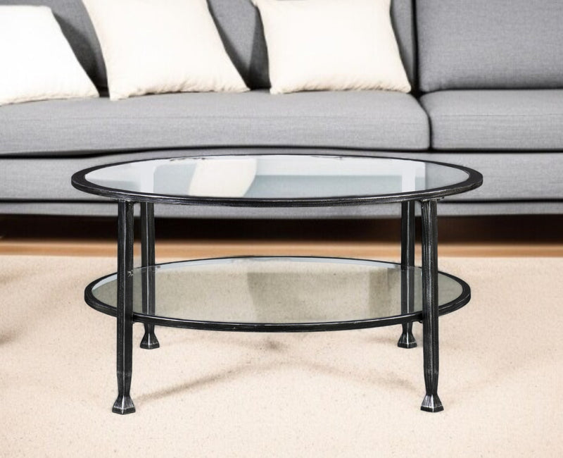 Round two-tier glass coffee table in front of a sofa, black metal frame