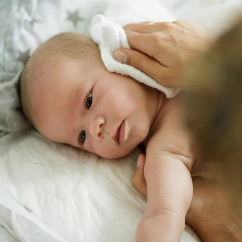 Baby boy with light brown hair being gently wiped with a soft white cloth, on a cozy gray star-patterned blanket.