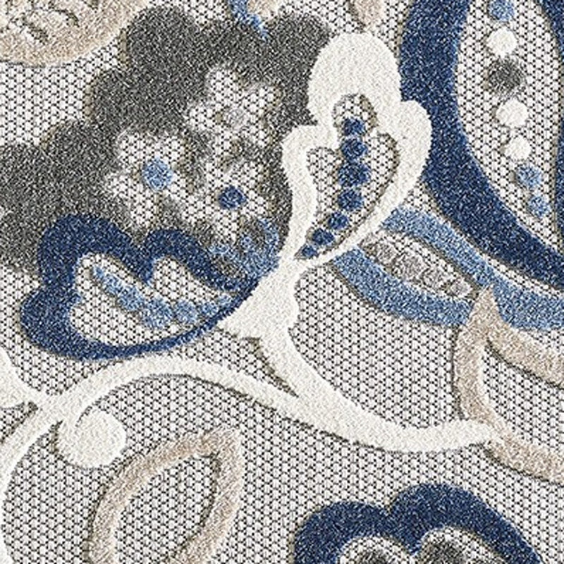Close-up indoor/outdoor area rug pattern: blue floral and gray swirling motifs on light base