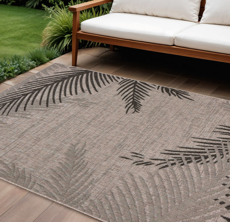 Beige indoor/outdoor area rug with black palm-leaf pattern and flat woven texture