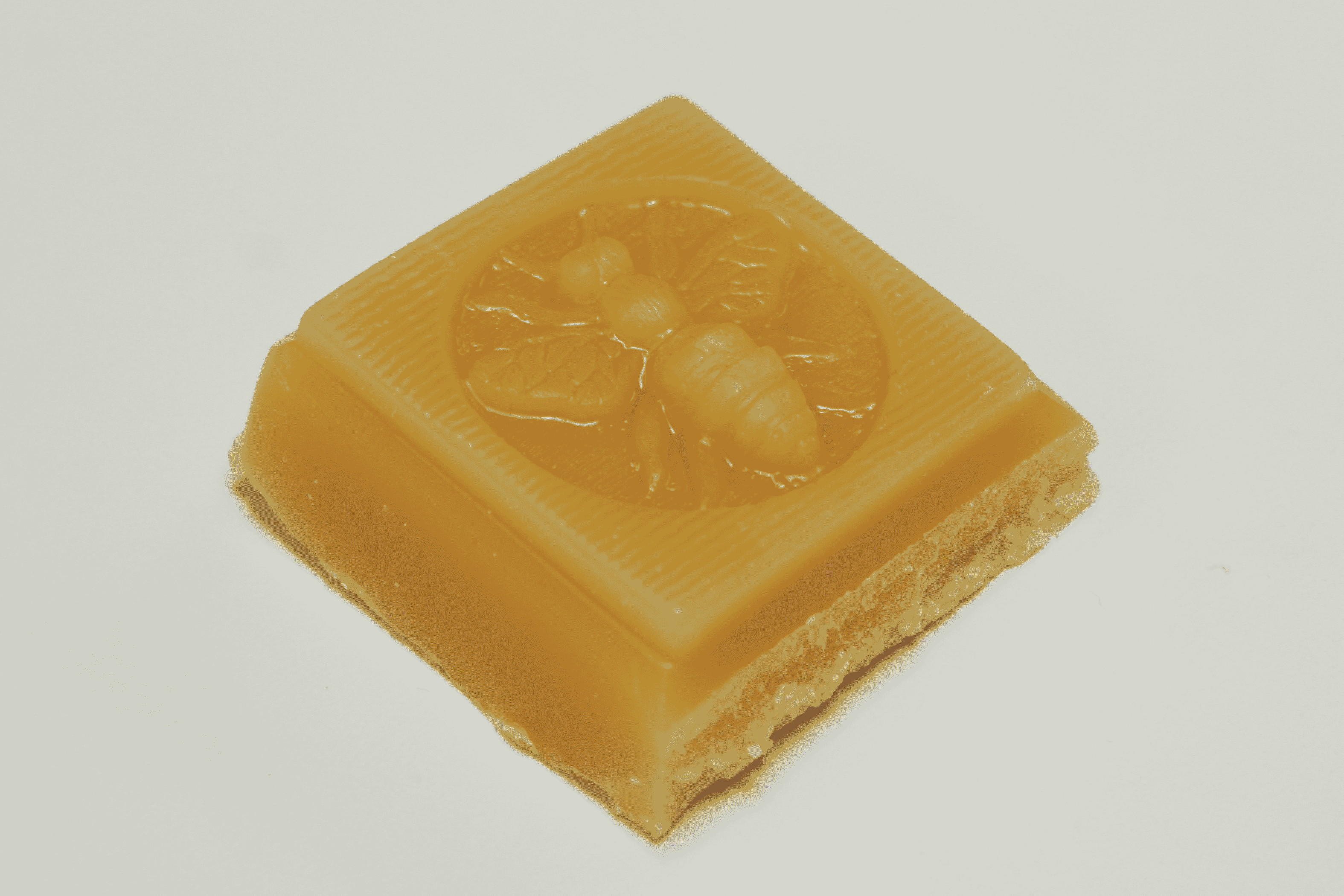 Amber beeswax soap bar with embossed flower-and-bee design and textured edges