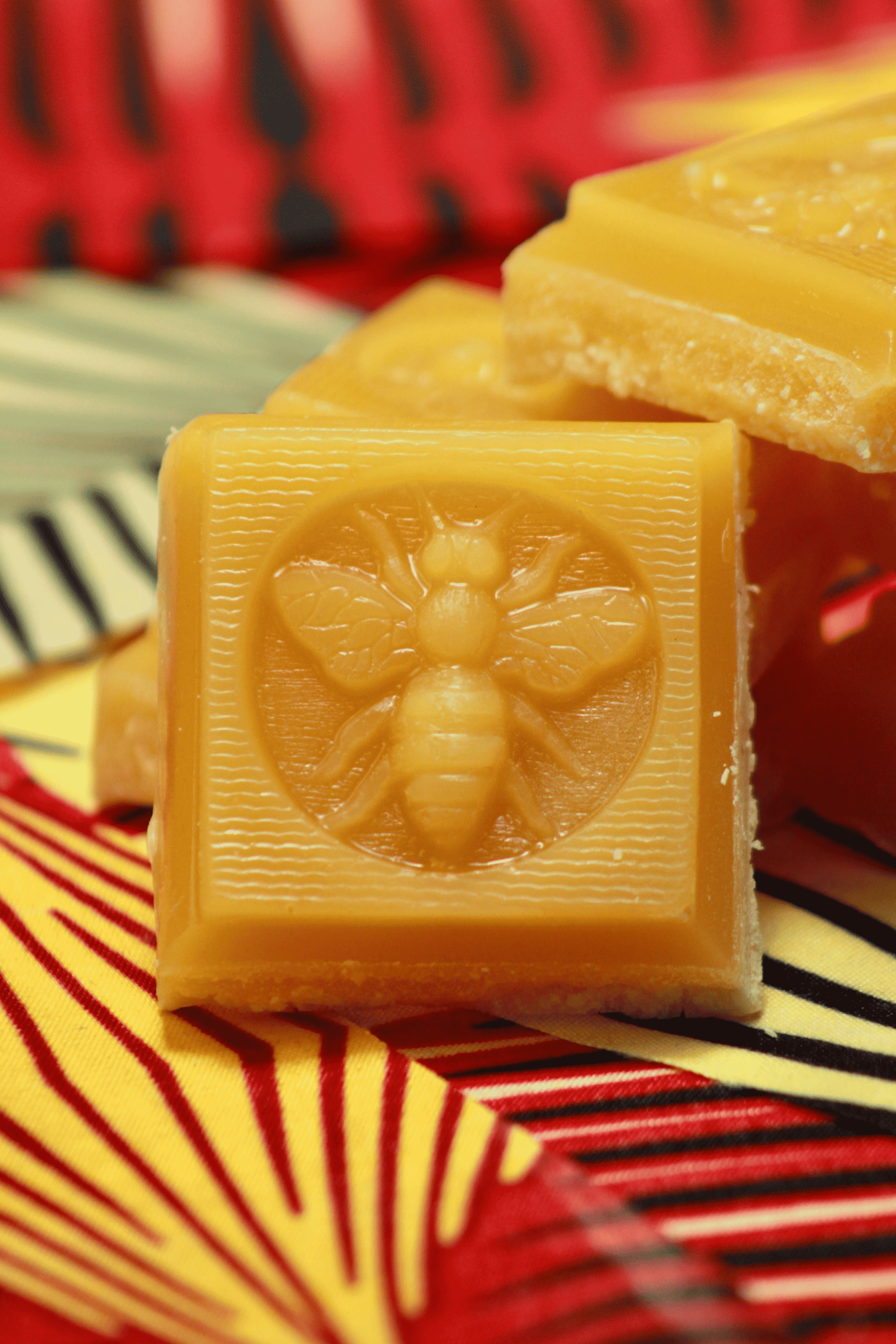 Amber beeswax soap bar stacked on patterned fabric, embossed flower-and-bee design