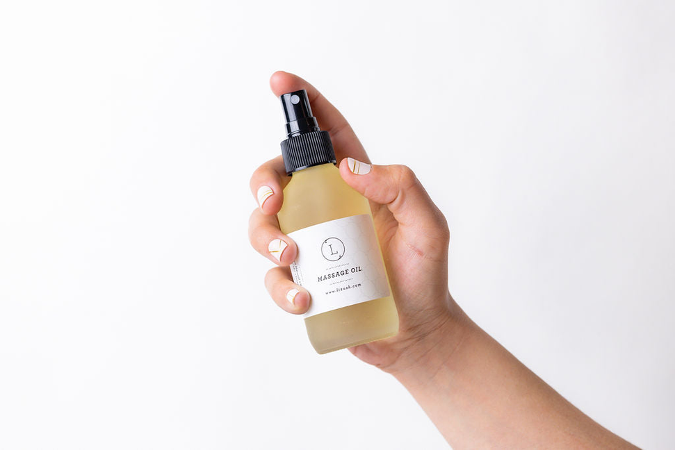 Massage oil dropper bottle held in hand with beige label, small glass vial