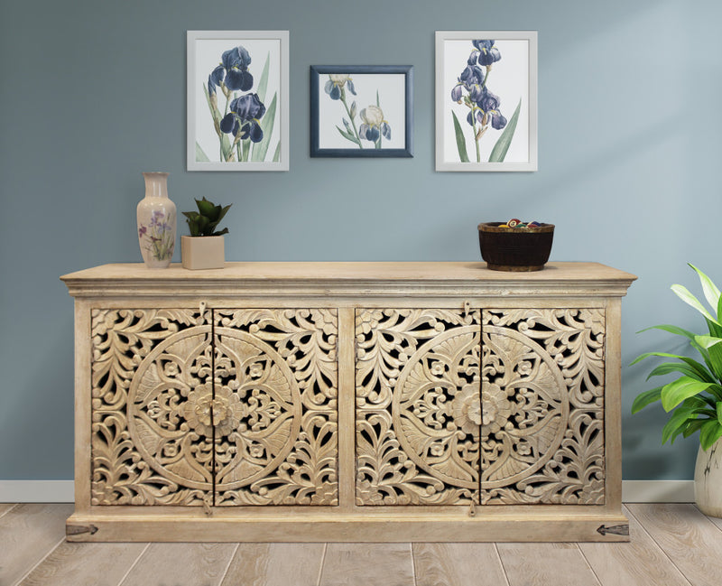 Beige distressed wood sideboard with four ornate carved doors, flat top, and feet.