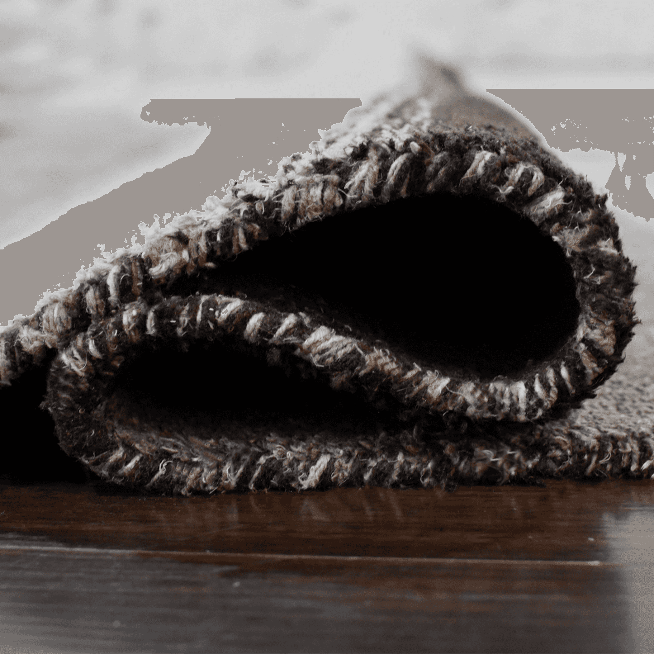 Rug corner detail with curved fold and stitched edge in dark brown, gray, and beige.
