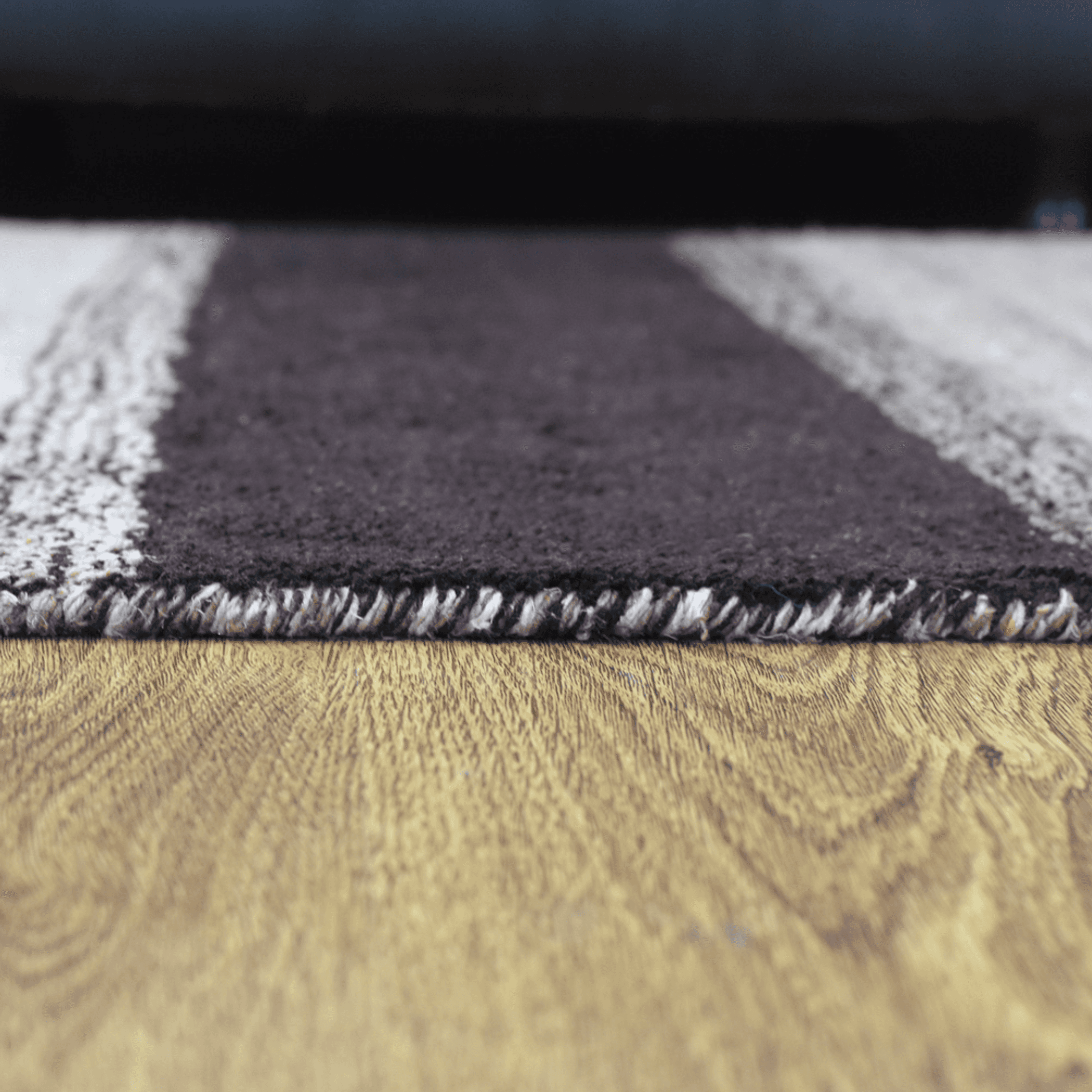 Rug edge detail with bound border and textured weave in dark brown and light gray.