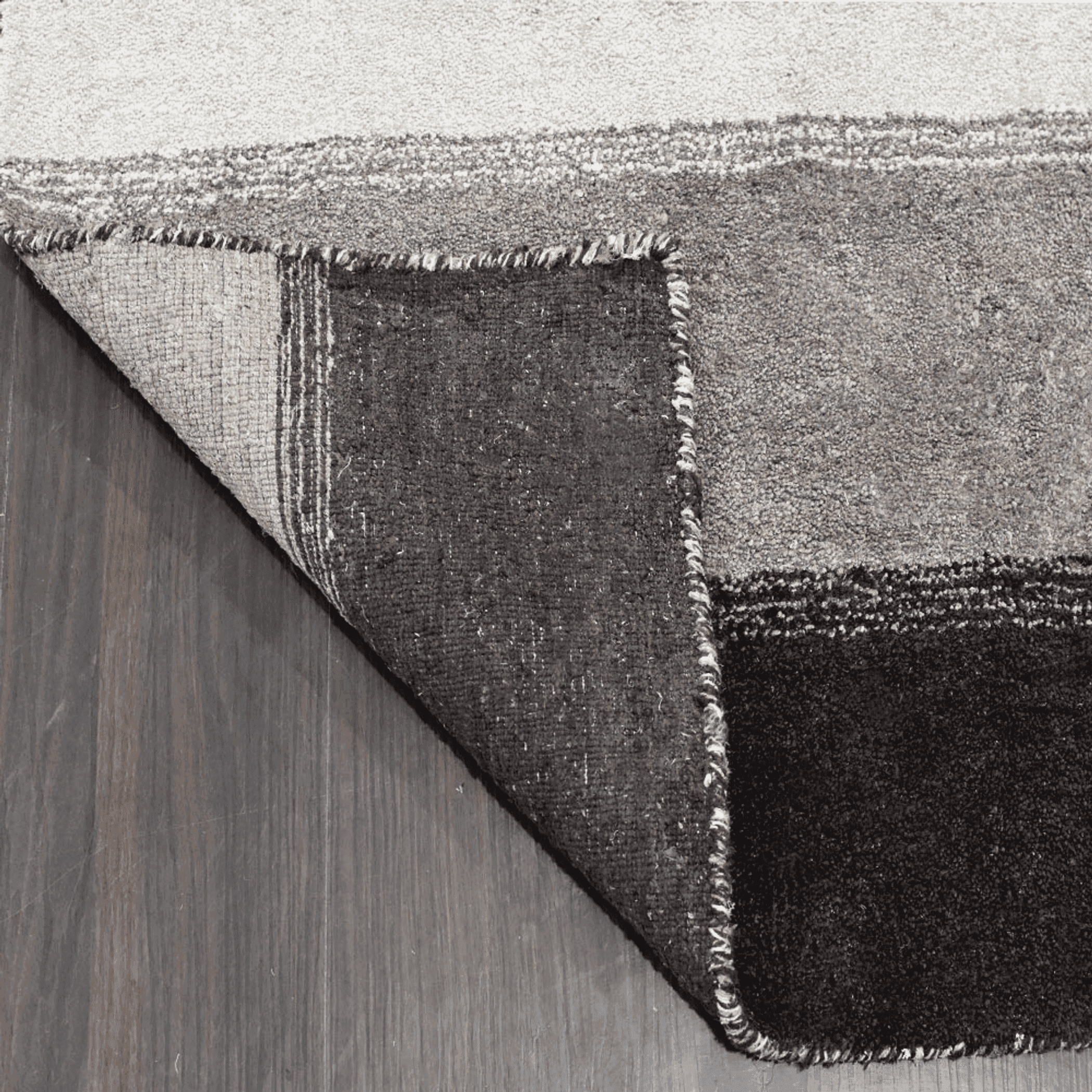 Rug corner view with visible backing and bound edge; stripes in charcoal and cream.