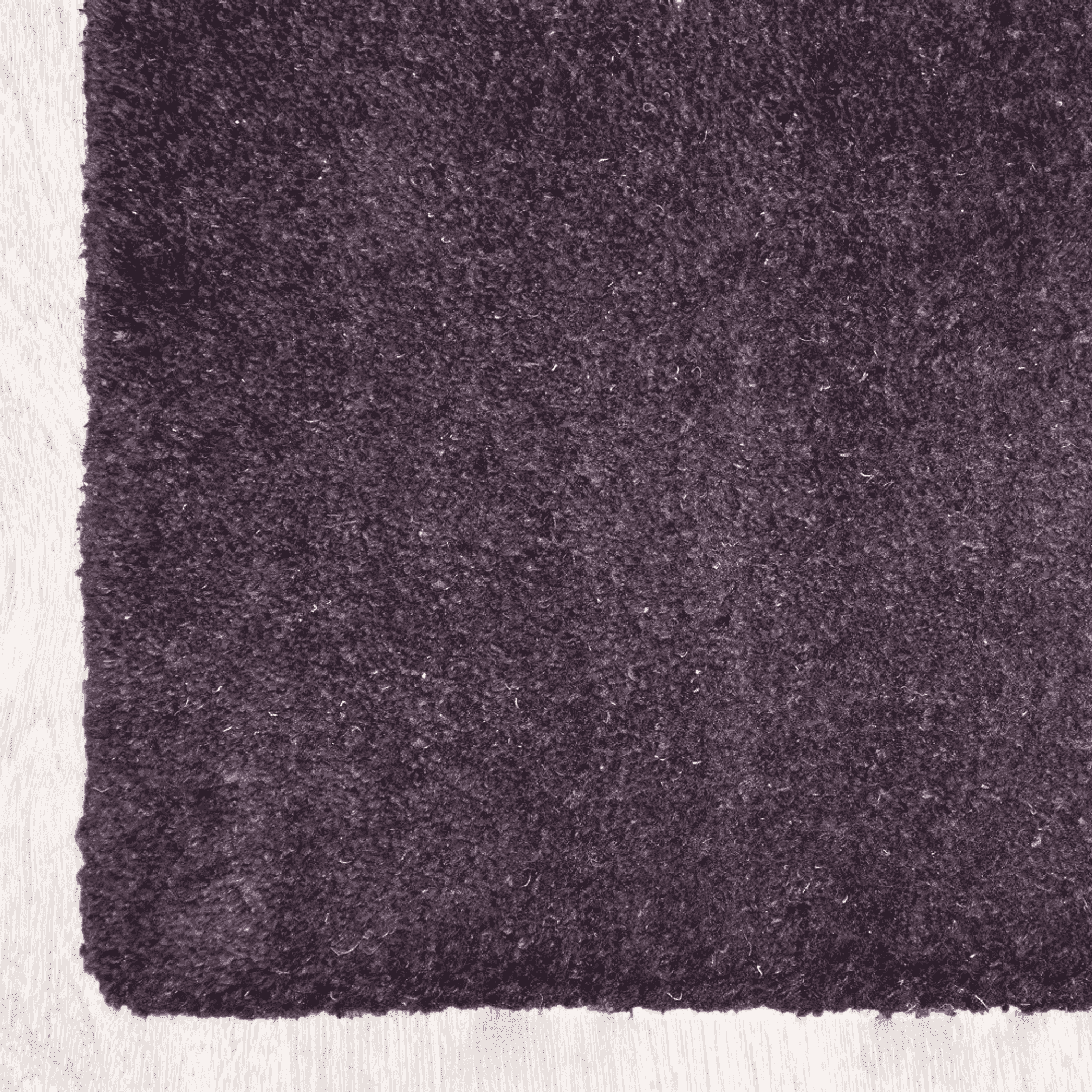 Corner of contemporary area rug in dark plum with dense textured pile and bound edge