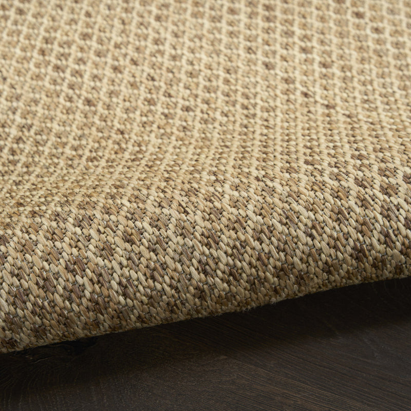 Close-up of tan woven rug texture with low pile and dark backing