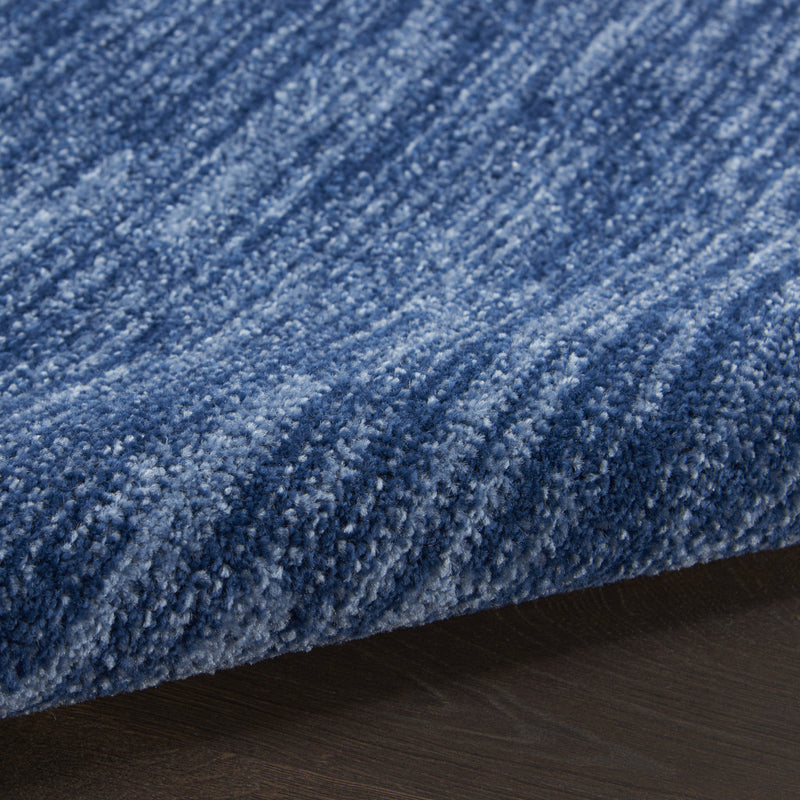 Close-up of blue rug pile showing dense fibers and mottled lighter specks.
