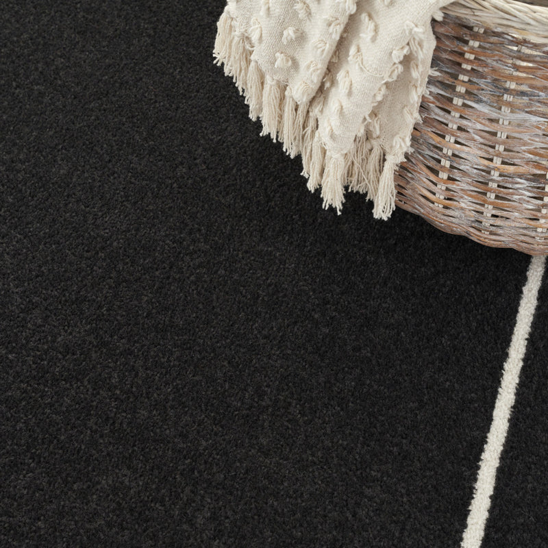 Black and ivory area rug corner with cream fringe edging and ivory border stripe.