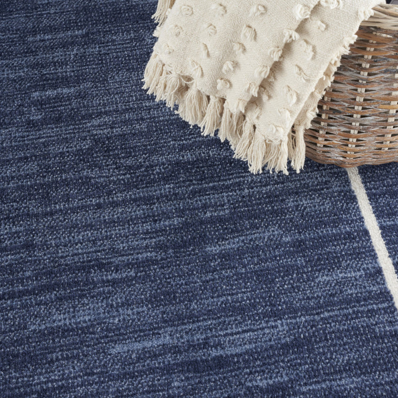 Navy rug close-up with ivory border lines and short ivory fringe corner