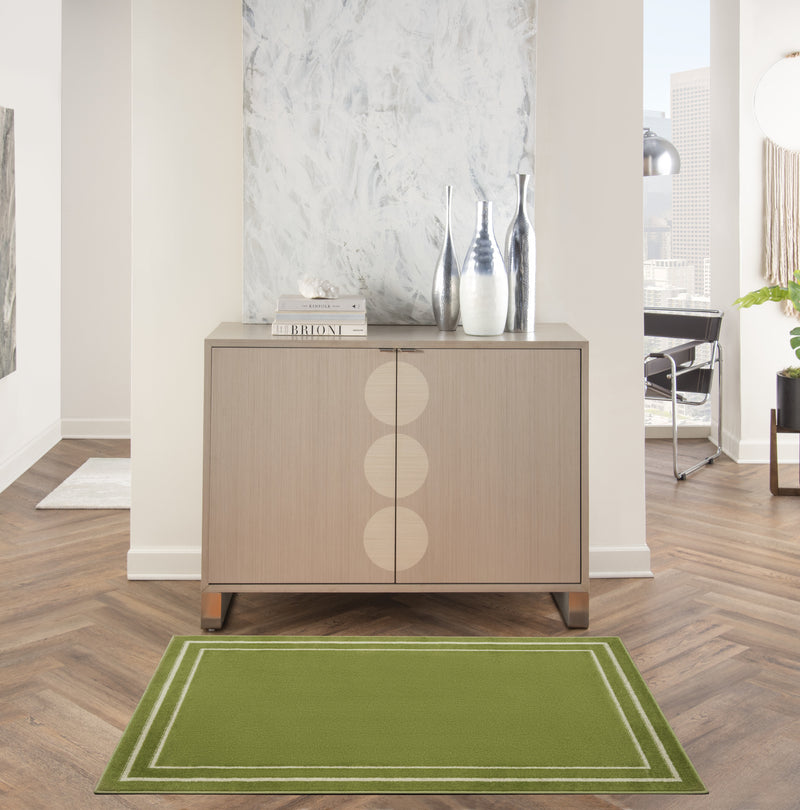 Green indoor area rug with ivory double border under a sideboard on wood flooring