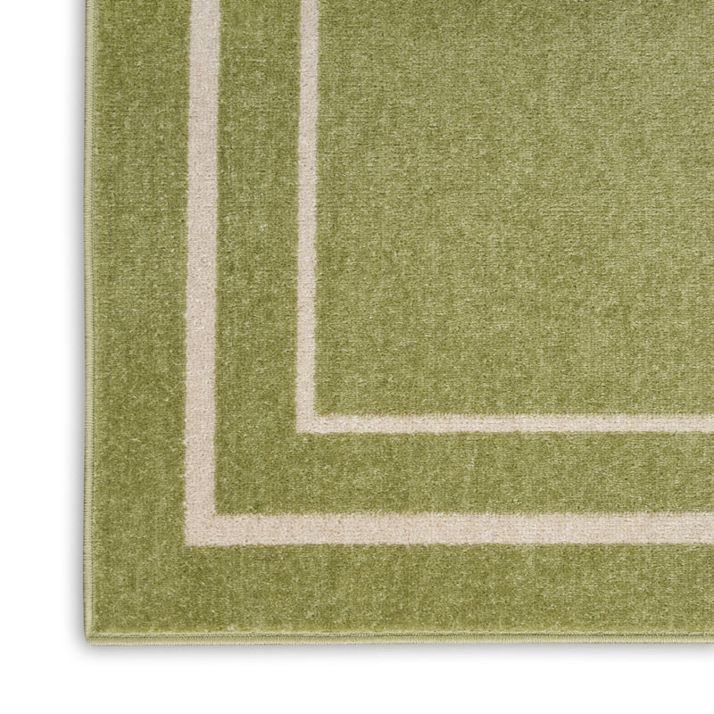 Close-up of green area rug corner with ivory inner frame and outline stitching