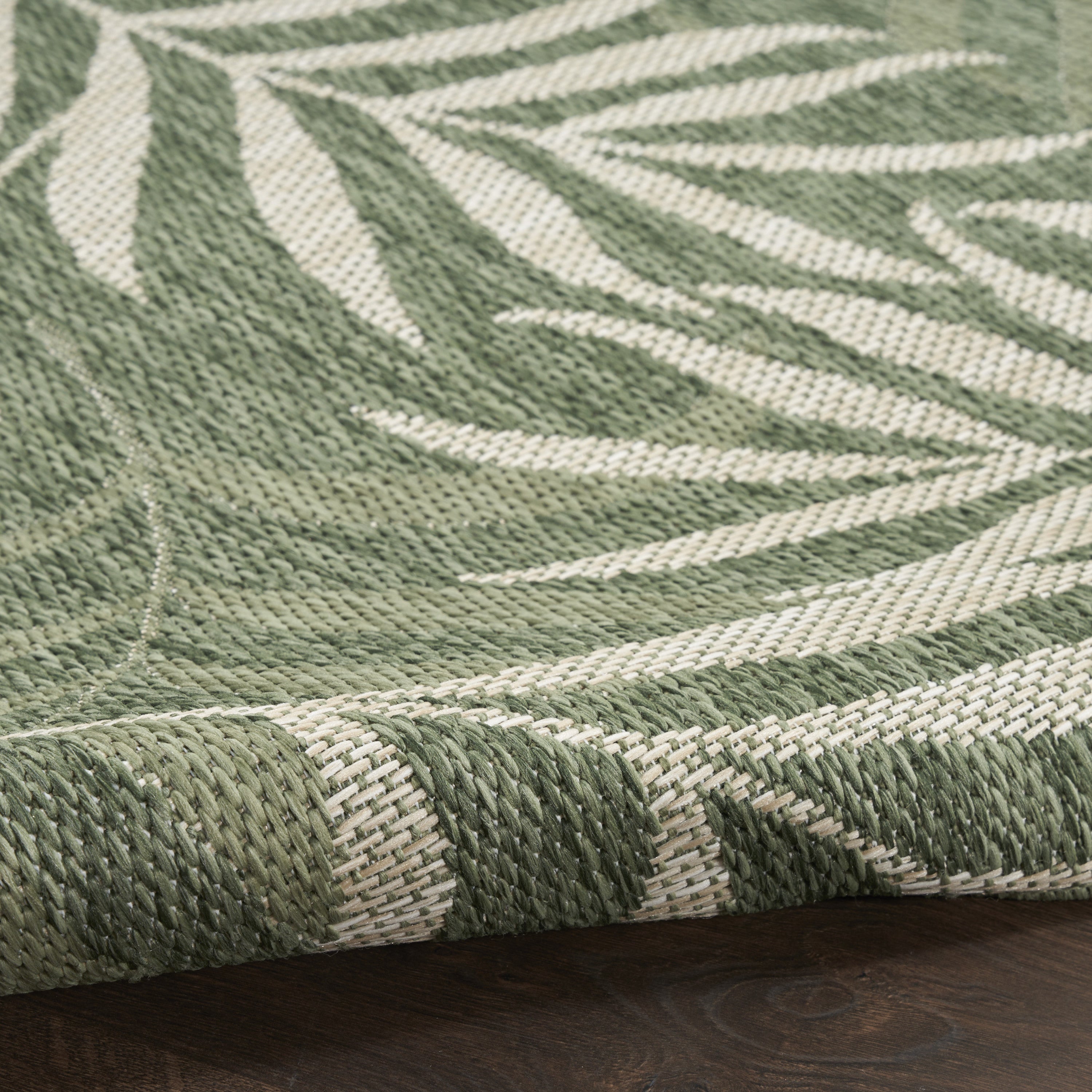 Green and ivory woven rug with palm leaf shapes and ivory stripe accents, close-up