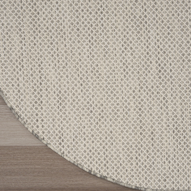 Round ivory area rug on wood floor with silver-tone geometric lattice and bound edge