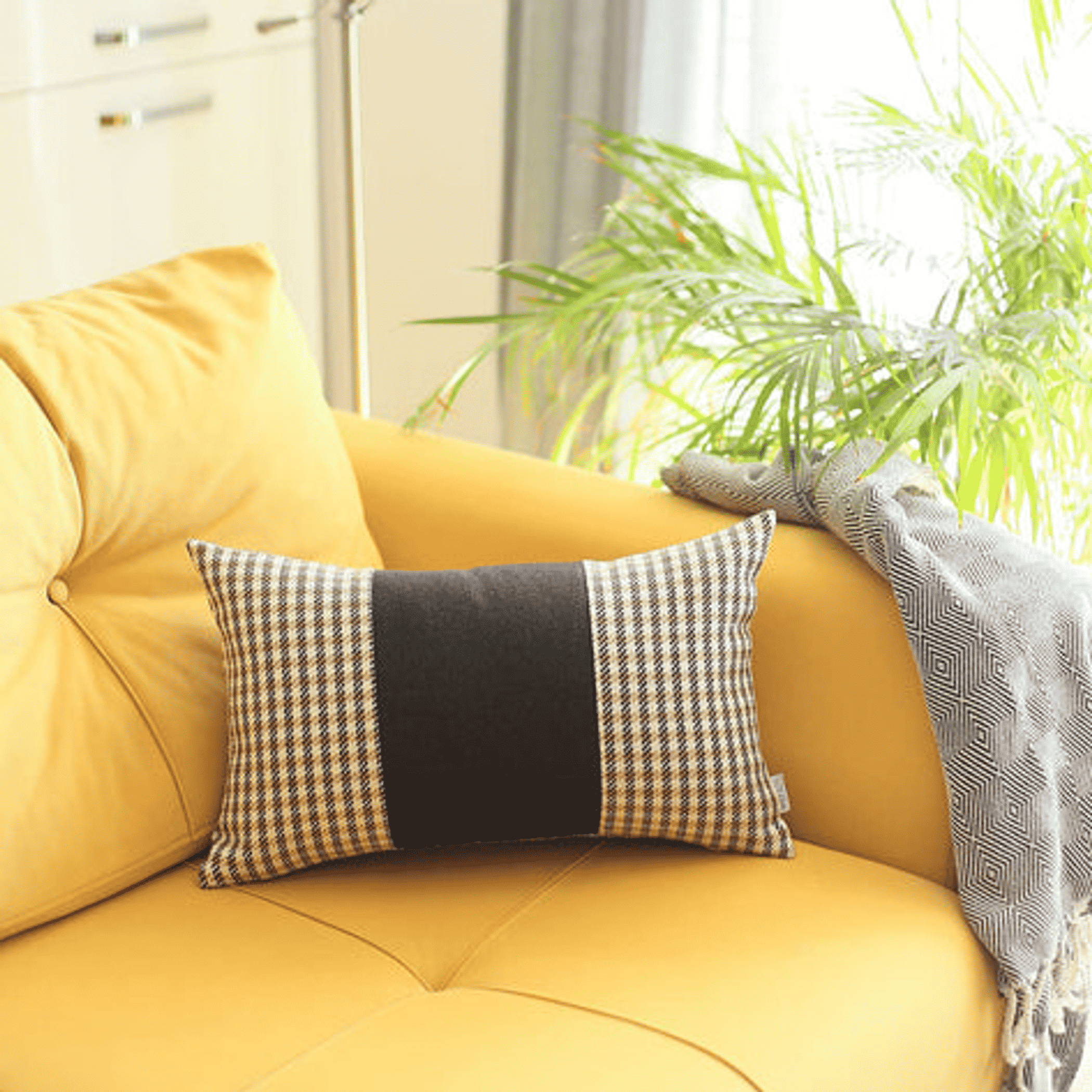 Rectangular throw pillow with black center panel and tan grid side panels on couch.