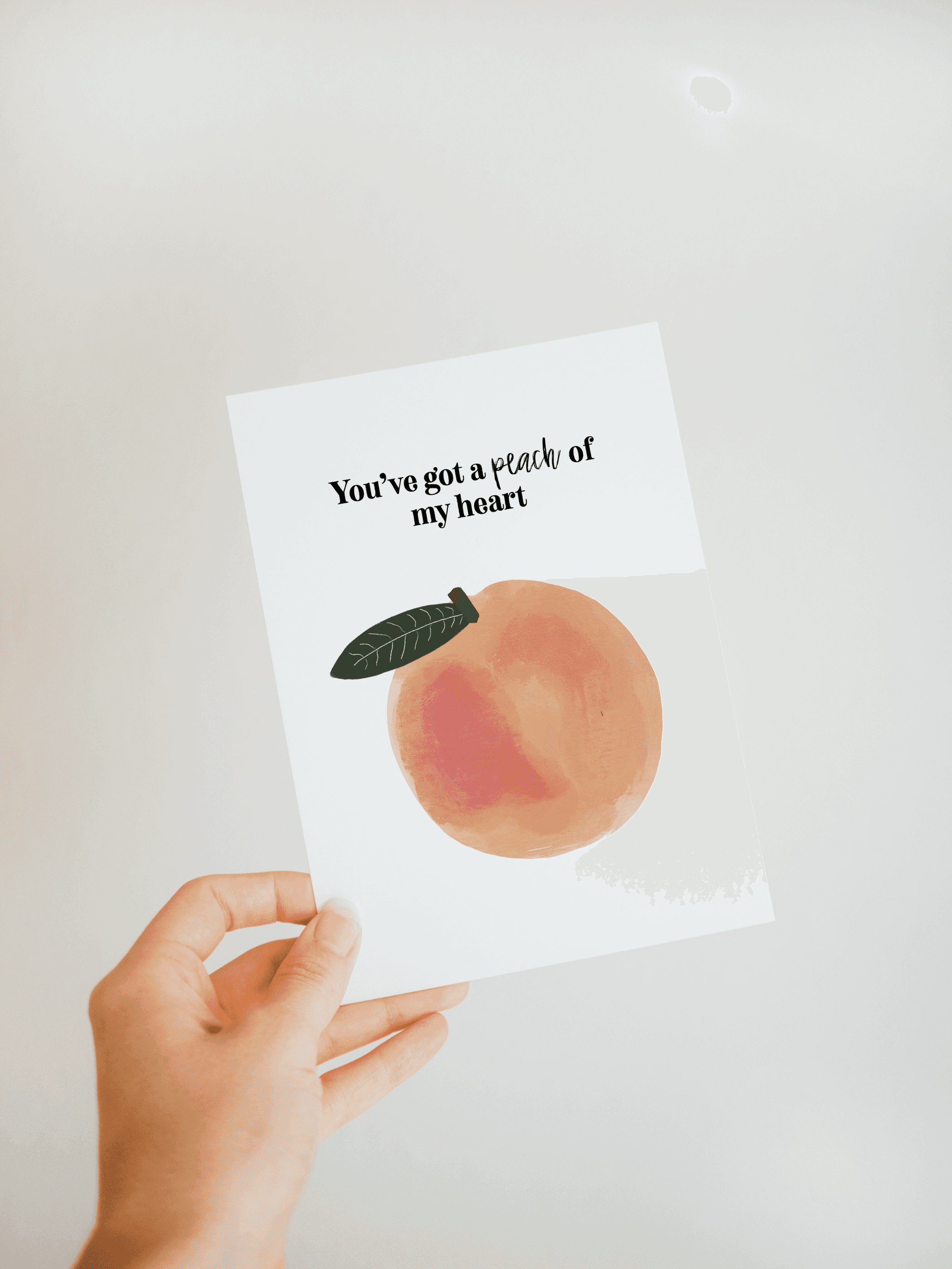 Hand holding greeting card with watercolor peach leaf and text: You've got a peach of my heart
