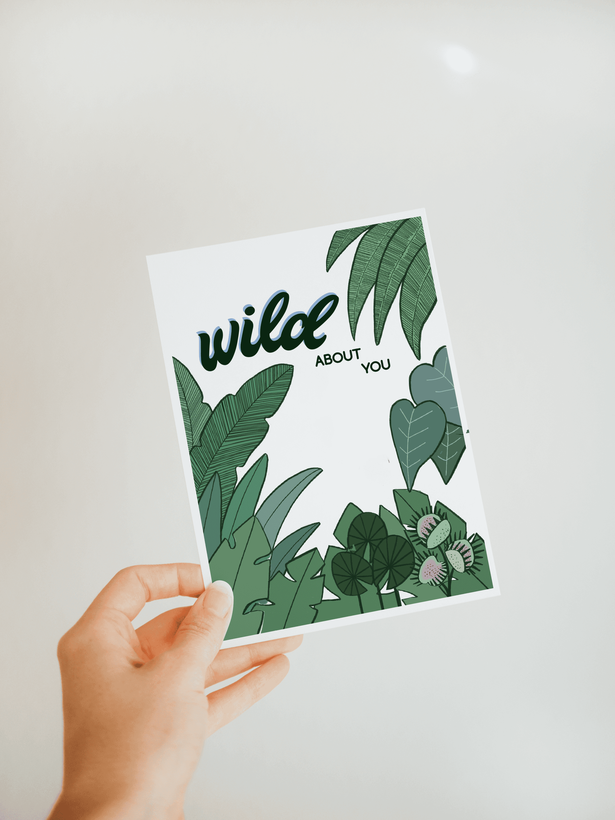 Handheld botanical greeting card with green leaf illustrations and text "wild ABOUT YOU".