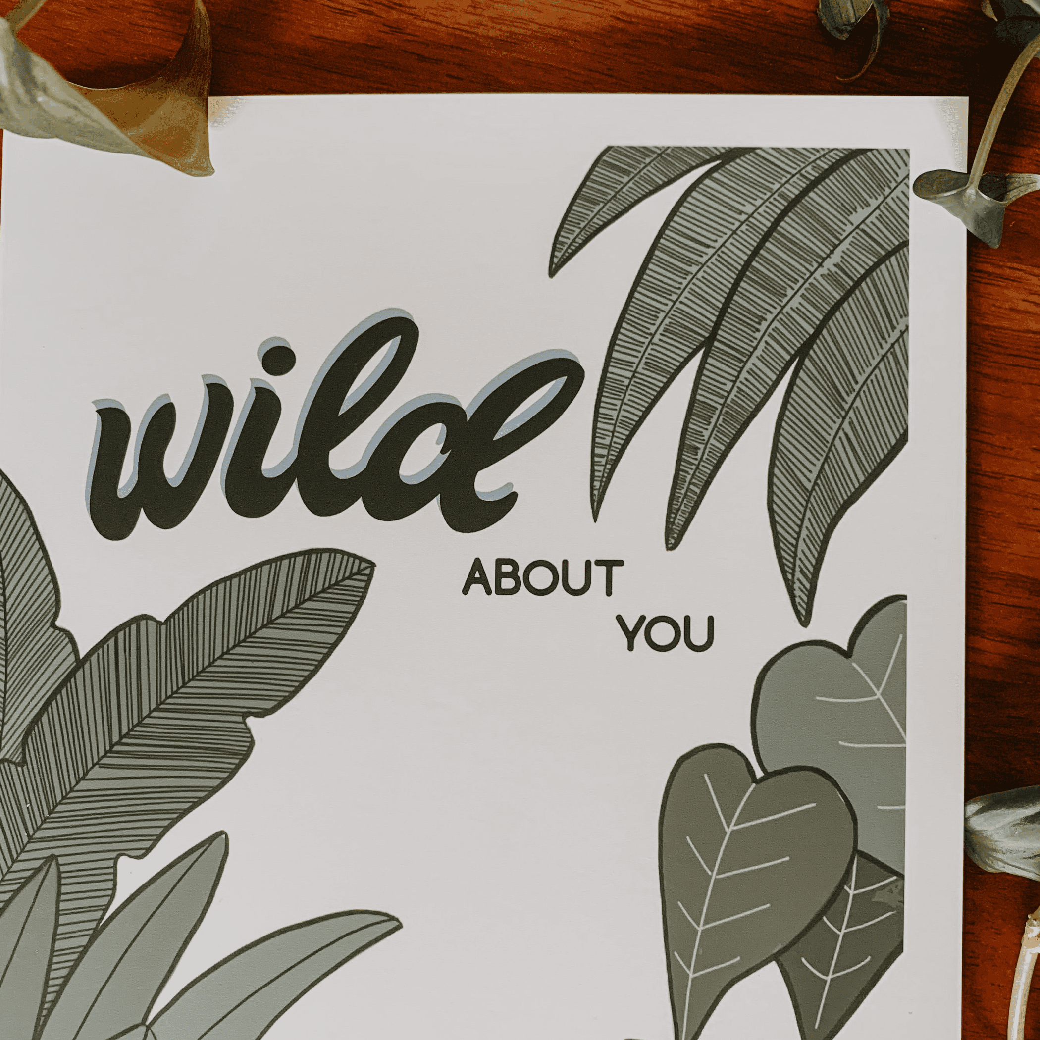 Botanical greeting card close-up showing "wild" script with leaf and heart-shaped foliage.