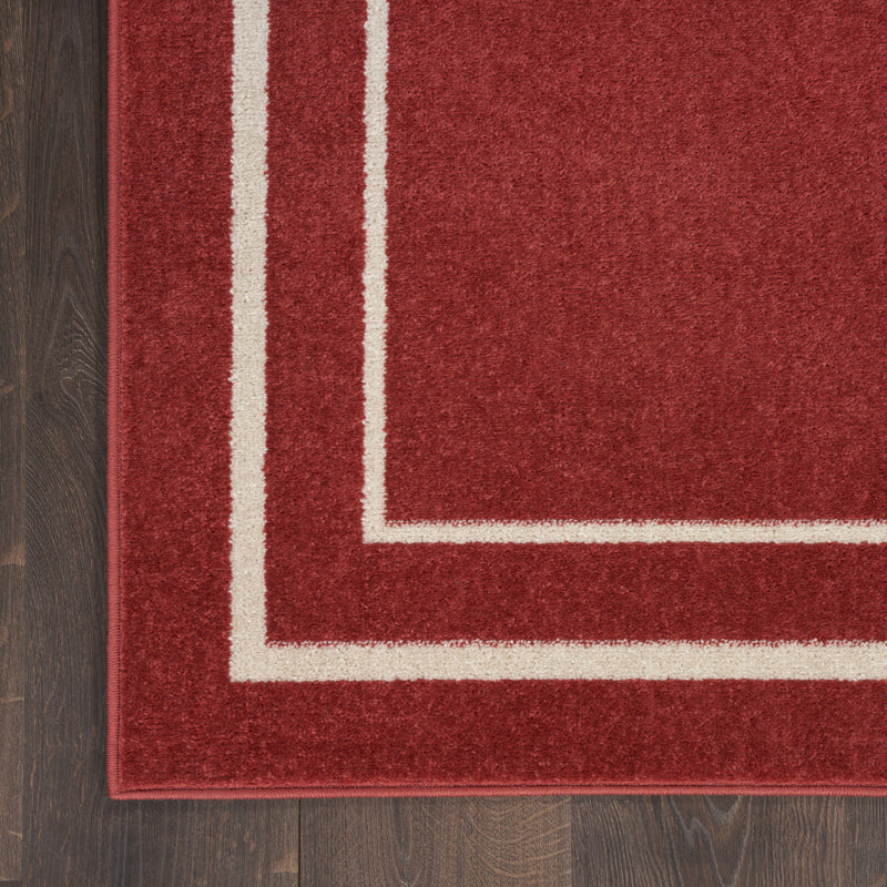 Corner close-up of red rug with ivory nested rectangle border and bound edge