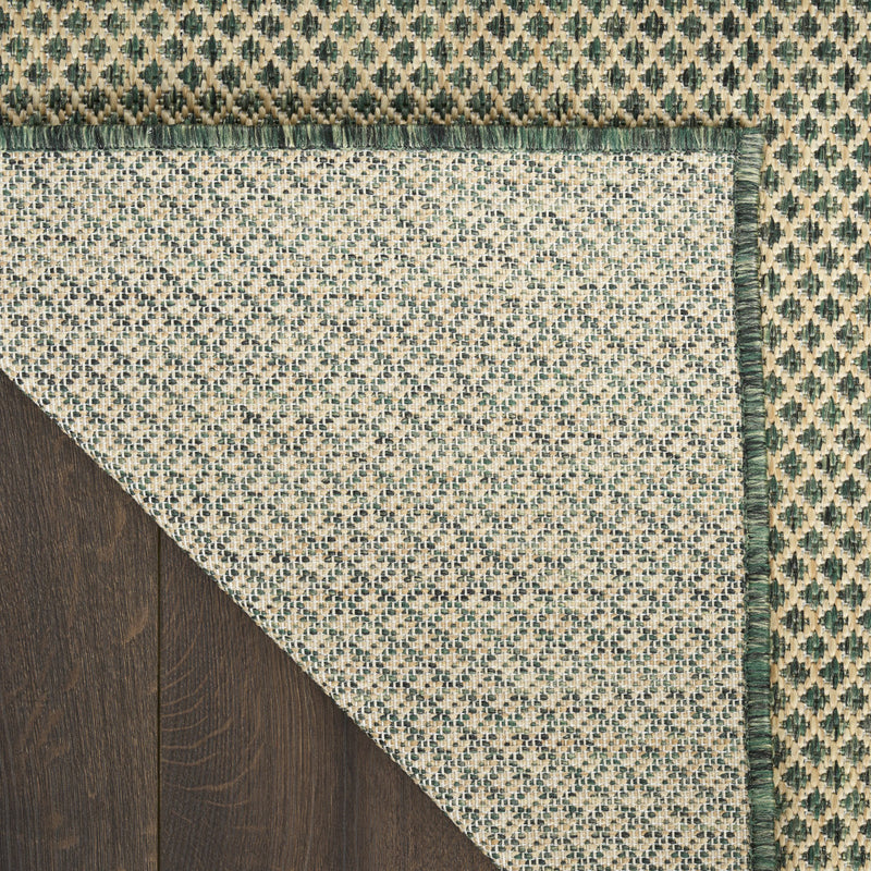 Rug corner view with green geometric border, speckled cream field, and fringed trim